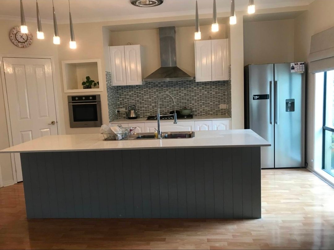 After open-plan kitchen makeover photo showing updated white cabinetry and a darker island finish